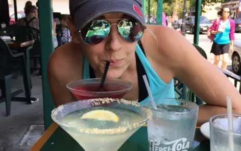 A woman drinking from a straw next to two drinks.