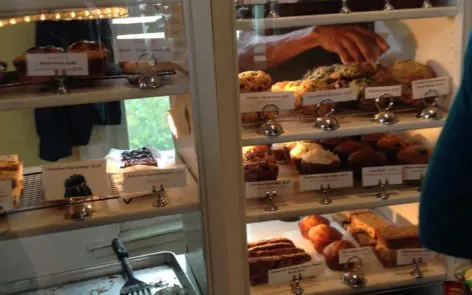 A person is reaching for some pastries in the display case.