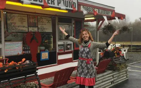 A woman standing outside of a restaurant with her arms in the air.