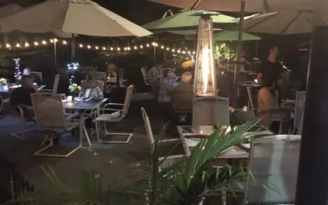 A patio with tables and chairs, umbrellas and lights.