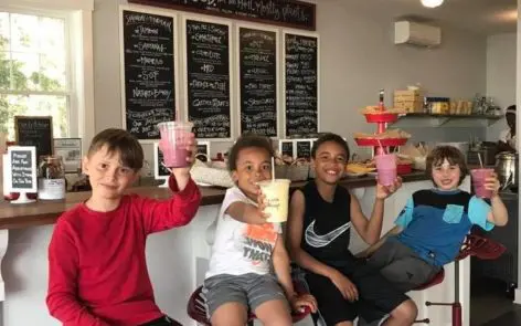 Three children sitting on a couch holding up drinks.