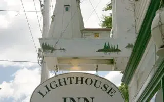 A sign for the lighthouse inn in front of a light house.