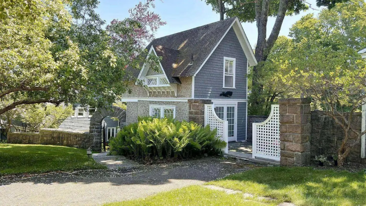 Charming gray two-story house with white trim and lush greenery.